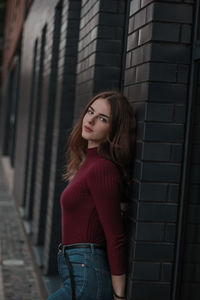 Portrait of beautiful young woman standing against brick wall