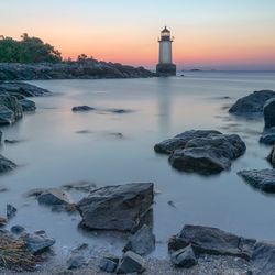 Lighthouse by sea against sky during sunset