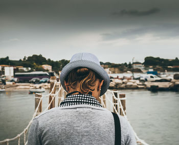 Rear view of woman standing by river against sky