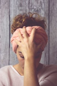Stressed young woman with head in hand against wooden wall