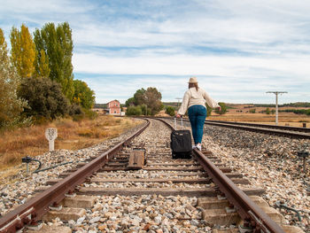 Rear view of woman walking with luggage on railroad track