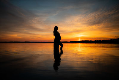 Silhouette woman standing on lake against sky during sunset