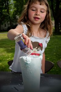 Close-up of cute girl preparing drink on table outdoors