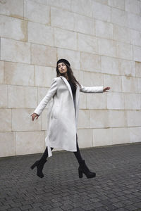 Young woman walking by wall on footpath