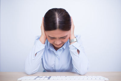 Businesswoman sitting with hands covering ears against wall