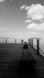 Empty bench on pier against sky