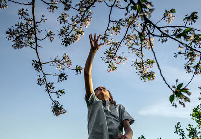 Low angle view of kid reaching the tree against sky