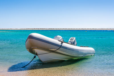 Boat moored on sea against clear blue sky