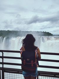 Rear view of woman looking at waterfall standing by railing
