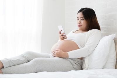 Young woman looking away while sitting on bed at home