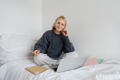 Young woman using laptop while sitting on bed at home