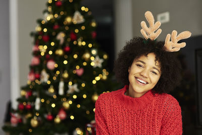 Portrait of smiling young woman standing against christmas tree