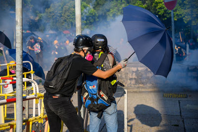 Rear view of people holding umbrella in city