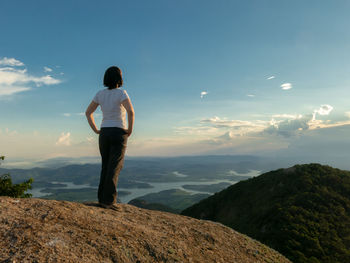 Rear view of man standing on rock against sky