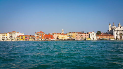 View of buildings by sea against clear blue sky