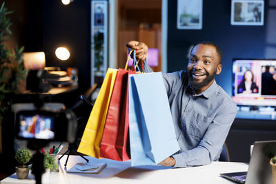 Portrait of young woman holding shopping bags while standing in office