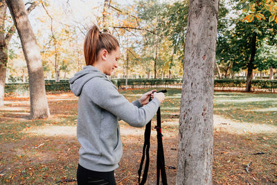 Happy woman exercising with straps while standing by tree