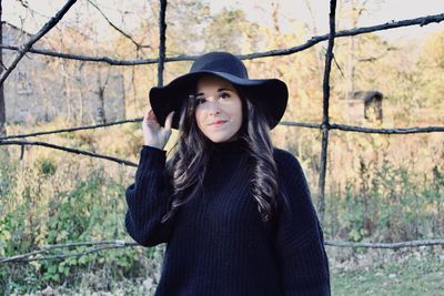 Portrait of beautiful young woman standing against trees