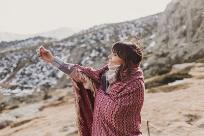 Side view of woman taking selfie while standing on mountain