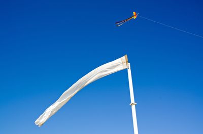 Low angle view of flag and kite against clear blue sky