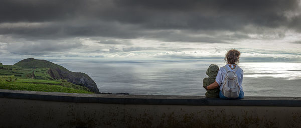 Woman sitting by sea against sky