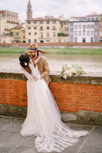 Couple embracing while standing by wall against building