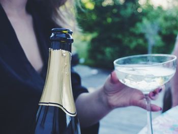 Midsection of young woman holding glass and wine bottle