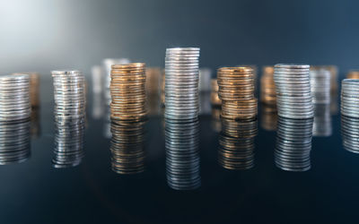 Piles of coins on a black, reflective surface seen from the top. inflation consuming our savings. 