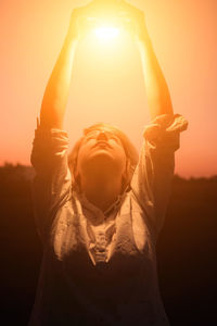 Midsection of woman standing against orange sky during sunset