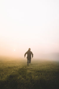 Rear view of man running on grassy field during foggy sunrise