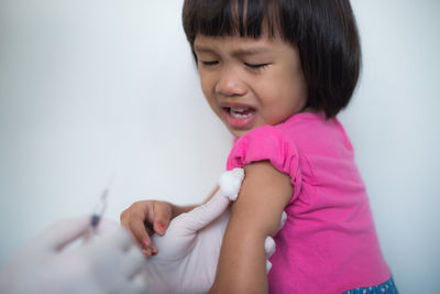 Cropped hands of doctor injecting crying girl at hospital