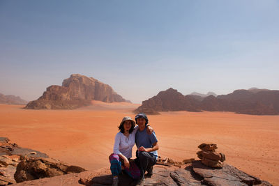 Portrait of woman and man sitting on rock at desert against sky