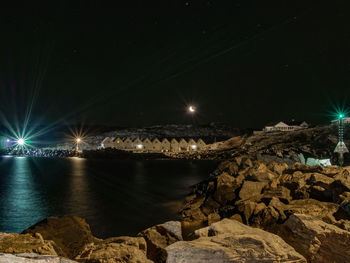 Illuminated rocks by sea against sky at night