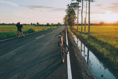 Man riding bicycle on road against sky during sunset