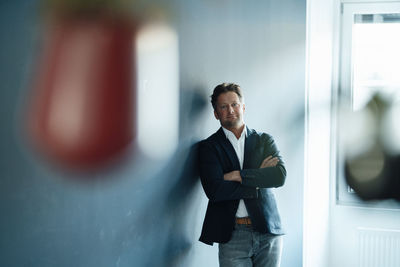 Mature businessman with arms crossed leaning on wall in office