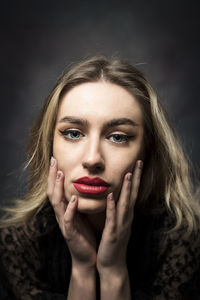 Portrait of young woman holding hear face with the hands against black background