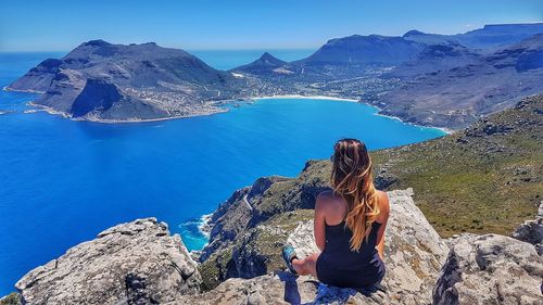 Rear view of woman sitting on rock looking at view