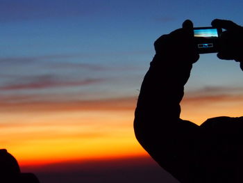 Close-up of silhouette man photographing against sky during sunset