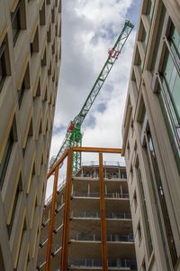 Low angle view of crane amidst building against sky