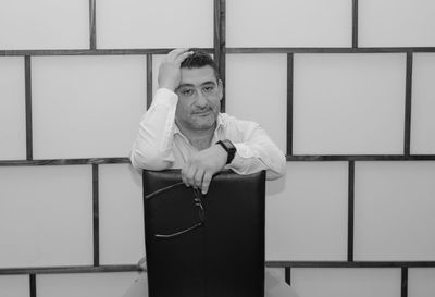 Portrait of thoughtful man sitting on chair against patterned wall