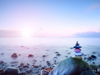 Balanced stone pyramide on shore of blue water of ocean. blue sky in water level mirror. 