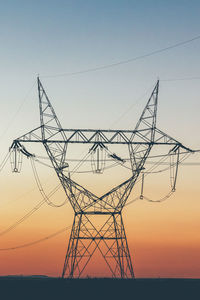 Low angle view of electricity pylon against sky during sunset