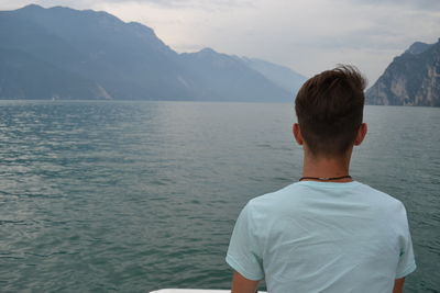 Rear view of man standing in sea against mountains