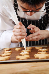 Cropped image of man icing on gingerbread cookies at table