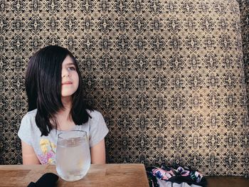 Young woman sitting on table against wall