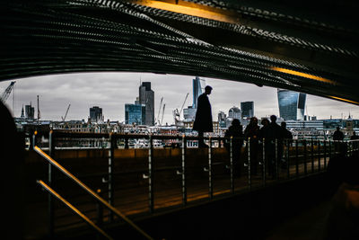 Silhouette people under bridge against cityscape