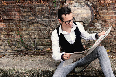 Retro-styled man reading newspaper outdoors.