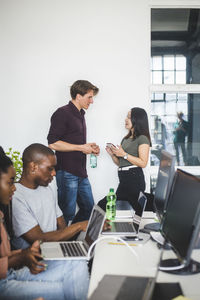 Colleagues talking by wall while computer programmers coding in office