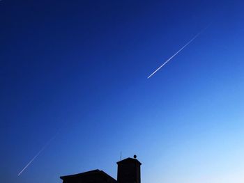 Low angle view of silhouette building and vapor trail against clear blue sky at dusk