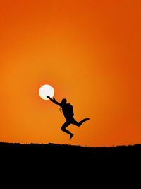 Silhouette man jumping against orange sky